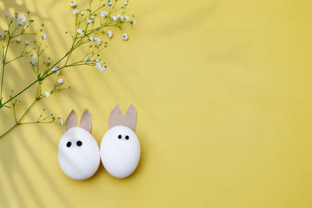 Easter scene with white eggs with rabbits ears over yellow background, palm shadows overlay. copyspace. Place for textの写真素材