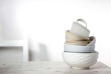 A pyramid of white bowls, plates and cups of different sizes and colors on a beige table in the kitchen. Scandinavian style. Place for your text. copy spaceの写真素材