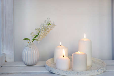 A white hyacinth in a 1970s fluted vase next to a tray of four lit candles is on the shelf. minimalism. Scandinavian style.の写真素材