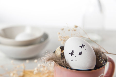 Easter concept. A white egg with copper wire ears and a painted rabbit sleeping face in a cup....