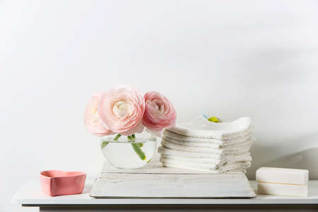 Three pale pink ranunculus in a transparent round vase and candles on the white windowsill. Rolled...