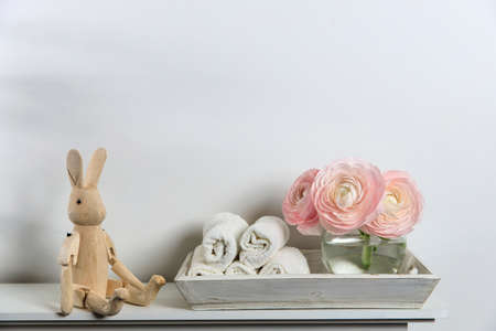 Three pale pink ranunculus in a transparent round vase and candles on the white windowsill. Rolled...