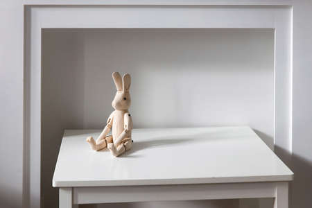 An unpainted wooden hare on hinges is on a white table in front of a fake fireplace. Place for textの写真素材