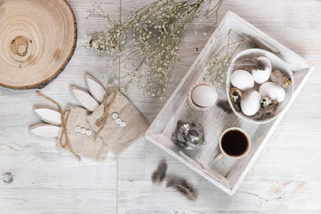 Table decorated for Easter in beige tones. Dried gypsophila, chicken and quail eggs, a silver...