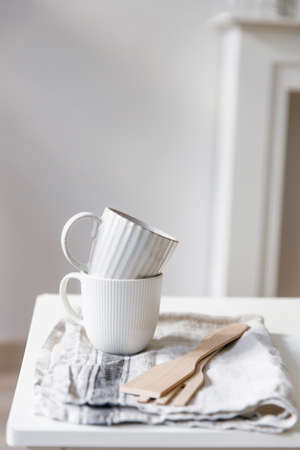 Two white mugs, a kitchen towel, a napkin and wooden frying utensils on the table. Defocus.の写真素材