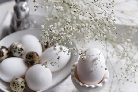 Table decorated for Easter in beige tones. Dried gypsophila, chicken and quail eggs, a silver figurine of a hare and a cup of coffee. Easter concept.の写真素材