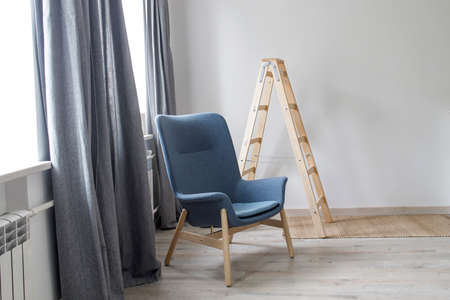 Room interior in Scandinavian style, in white and gray tones. A gray armchair with wooden legs by...
