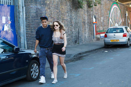 London, UK - 17 June 2019, A young man in a cap hugs a girl in a short skirt and glasses