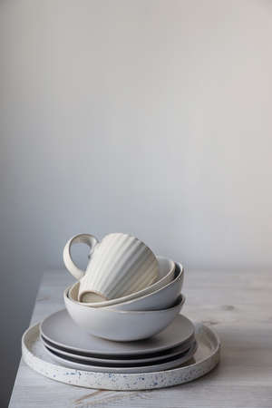 A pyramid of white bowls, plates and cups of different sizes and colors on a beige table in the...