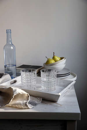A blue transparent water bottle and two ribbed glasses on a white wooden tray on the kitchen table.の写真素材