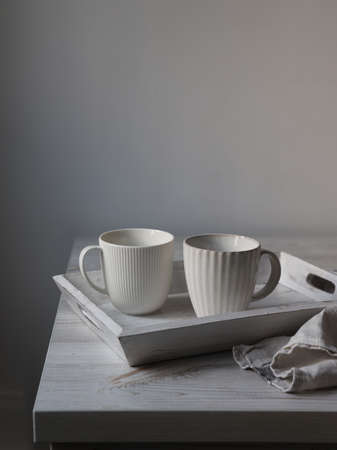 Two corrugated mugs on a white tray and a kitchen towel on a beige table against a white wall....