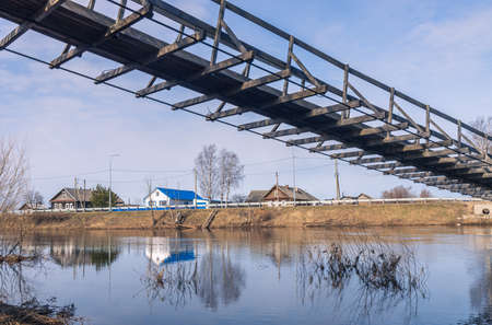 Verkhovye, Olonetsky district, Karelia, Russia, - April 28, 2022, Narrow wooden pedestrian suspension bridge across the river in russian village near Olonets. Sunny summer evening.の写真素材