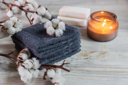 Four gray terry face towels, two bars of soap, a candle in a glass jar, and a branch of cotton at the spa. Beauty saloon. Comfort and careの写真素材