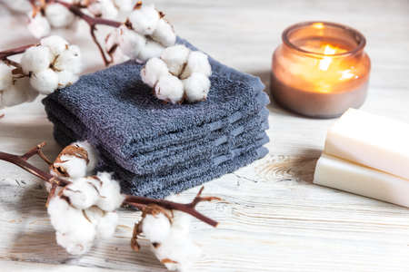 Four gray terry face towels, two bars of soap, a candle in a glass jar, and a branch of cotton at the spa. Beauty saloon. Comfort and careの写真素材