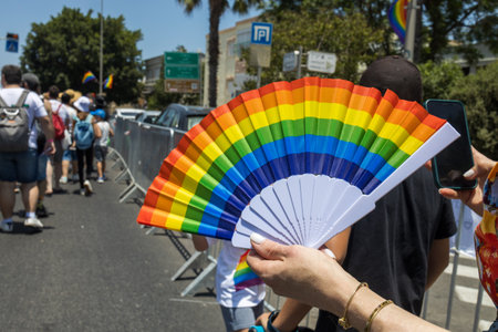 Haifa, Israel - June 24, 2022: People with protest signs in preparation to the annual LGBTQ pride parade. Fan in the form of a rainbowのeditorial素材