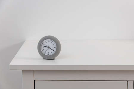 A round gray clock shows twenty past nine on a white chest of drawers.