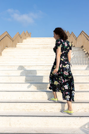 A twenty-year-old girl in a black dress with yellow flowers climbs the marble stairs
