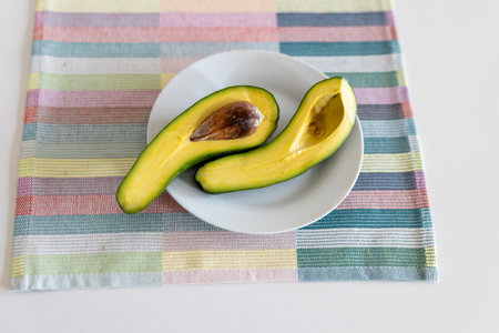 A cut avocado into two halves on a plate on a napkin on a white table. Place for text