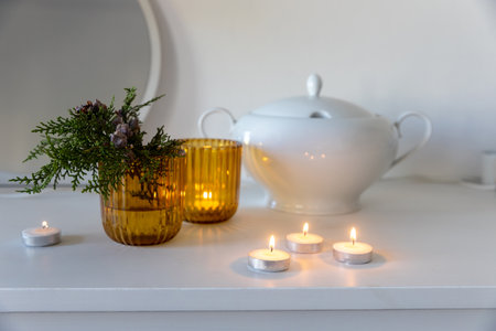 Yellow glass candlesticks, a branch of arborvitae with cones, a white porcelain tureen on a chest of drawers decorated for Christmas.の写真素材