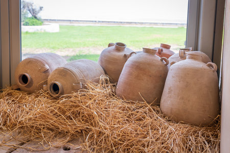 Clay jugs, amphorae and water vessels on straw near a glass window