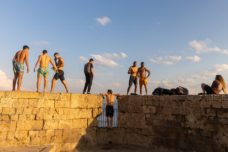 Acre, Israel - November 01, 2022, Young people on the wall of the ancient city, going to jump into the seaのeditorial素材