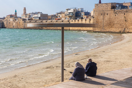 Acre, Israel - January 08, 2023: Sunset view of the Horses beach, the sea wall and the fishing port, with locals and visitors, in the old city of Acre (Akko), Israelのeditorial素材