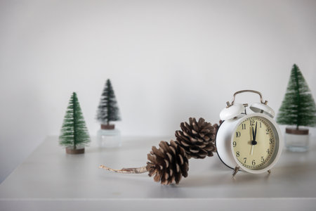 A white alarm clock, a twelve pointer, a small artificial green Christmas tree on a white chest of drawers. Copy space. Christmas card.の写真素材