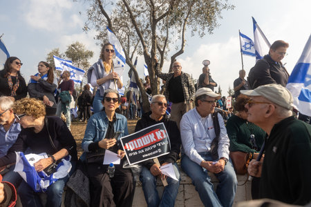 JERUSALEM, ISRAEL - February 20 2023: Israelis protest near the Knesset against plans by prime minister Benjamin Netanyahu new government to trample the legal. People with flags sit on the stepsのeditorial素材
