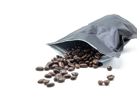 Black vacuum bag for coffee from which coffee beans spill out. Isolated on white.の写真素材
