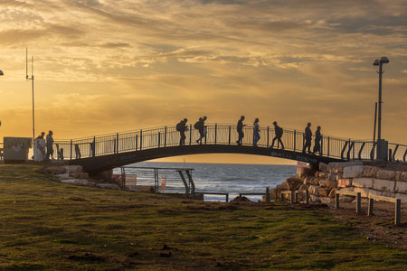Tel Aviv Israel - 07 March 2023, A small footbridge near the embankment. People walk along the bridge in the backlight. Silhouettes.のeditorial素材