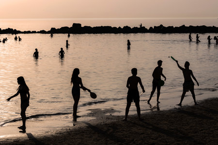 Tel Aviv Israel - 07 March 2023, A group of teenagers play badminton against the backdrop of the setting sun on Dado Beach. Silhouettesのeditorial素材