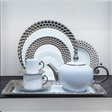 An antique white with silver porcelain service - a teapot, two cups and plates - stands on the chest of drawers.の写真素材