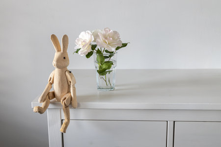 Tea white rose in a transparent glass on a white table. There is a wooden hare on hinges. Place for text.の写真素材