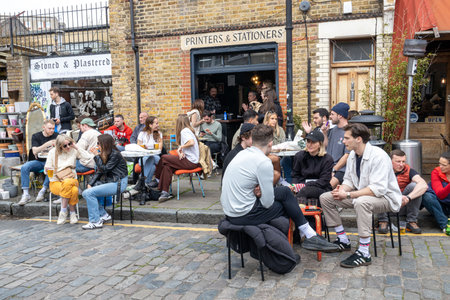 London, UK - April 17, 2023: Columbia Road Flower Sunday market. Local drink coffee and alcohol while sitting on the sidewalk in good weatherのeditorial素材