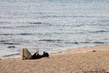 Haifa, Israel - March 1, 2023, Unidentified man sitting on stones, reading a book, overlooking the seaのeditorial素材