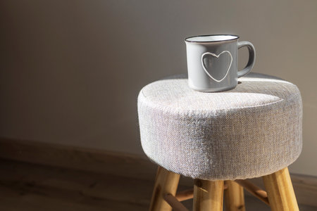 A gray ceramic enamel mug with a heart stands on a soft ottoman