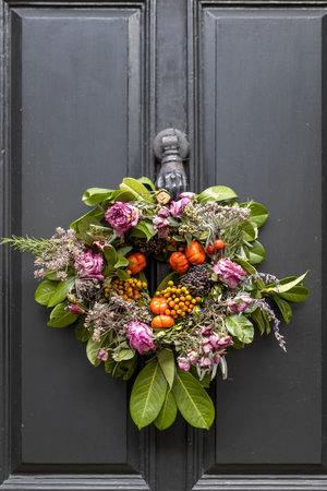 A Christmas wreath of dried red roses, faux pumpkins, dill sprigs, seeds, laurel branches, dried tree branches, eucalyptus and plants adorns the front door.の写真素材