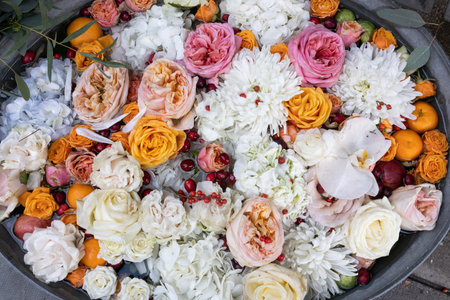 Pink and orange roses, blue hydrangea, red cranberries, white chrysanthemums, tangerines in water in...