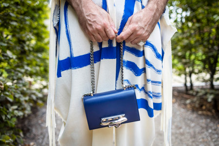 A small blue baby bag made of genuine leather on a silver chain is held by men's hands. Against the...