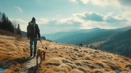 A man with a boxer dog and a backpack goes to the mountains. Spring, yellow grass and not yet melted snow. There are mountains on the horizon.の写真素材