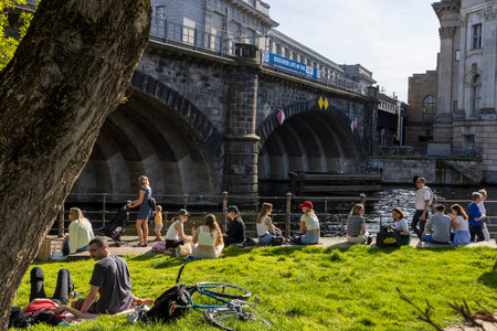 Berlin, Germany - 02 April 2024, People are sitting on the embankment. Spring in Berlin. A pleasure boat with groups of cheerful people is sailing along the canal.のeditorial素材