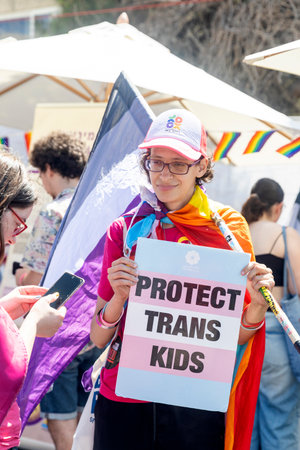 Haifa, Israel June 21, 2024, Pride. A young man wrapped in a trans flag stands with a sign reading "Protect Trans kids" in the crowd.のeditorial素材