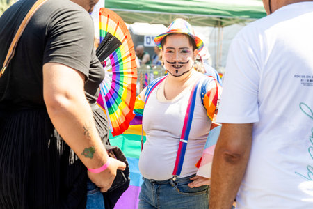 Haifa, Israel June 21, 2024, Pride Parade. Drag queer in a hat with rainbow symbols with a painted mustache and beard, in a white T-shirt with suspenders poses.のeditorial素材