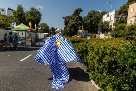 Haifa, Israel June 21, 2024, Pride Parade. A man wearing a cape made of the Israeli flag and a yellow ribbon on his back - a symbol - remember the hostages, runs down the street.のeditorial素材