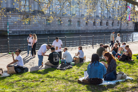 Berlin, Germany - 02 April 2024, People sit on the embankment near the museum island, a boat sails along the canal - spring in Berlin. Young women and young men spend time togetherのeditorial素材