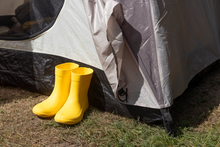 Yellow boots standing near a tent in a campsite in a pine forest.