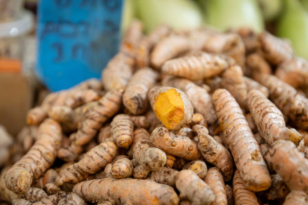 A pile of turmeric roots heaped on a stall for sale. One of them is cut open.の写真素材