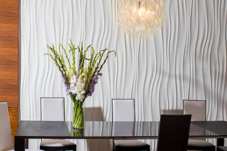A bouquet of white and purple gladioluses stands in a tall vase on a desk opposite a textured white wall. Conference room.の写真素材