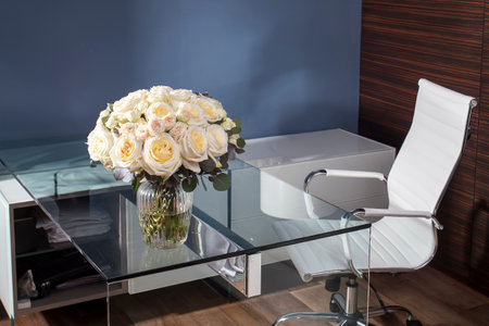 A bouquet of large white-yellow roses and small pink roses with eucalyptus branches in the interior of a home office.の写真素材