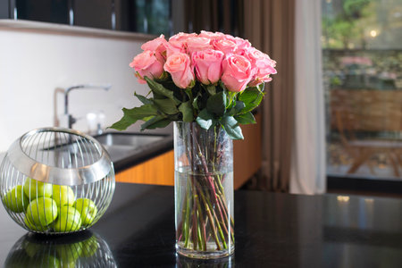 A bouquet of red roses on the kitchen table. Next to it, a metal vase with green apples. Reflection on the polished table.の写真素材